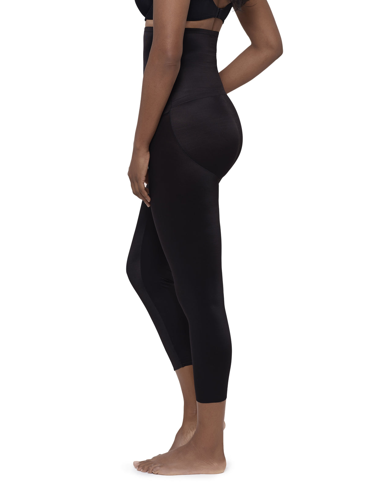 A side-profile view of a model wearing high-waisted black shapewear leggings against a plain white background.
