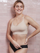 a woman standing next to a pink wall wearing a nude shaping wireless bra bralette all-groups