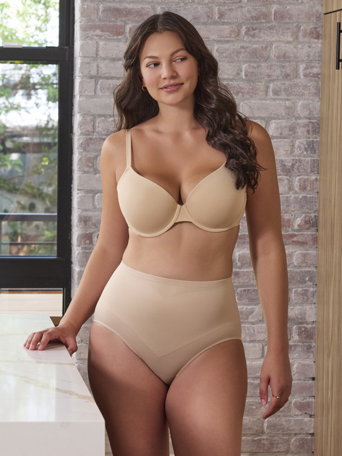 a woman waking around a kitchen while wearing a beige tummy control panty shape brief shapewear all-groups